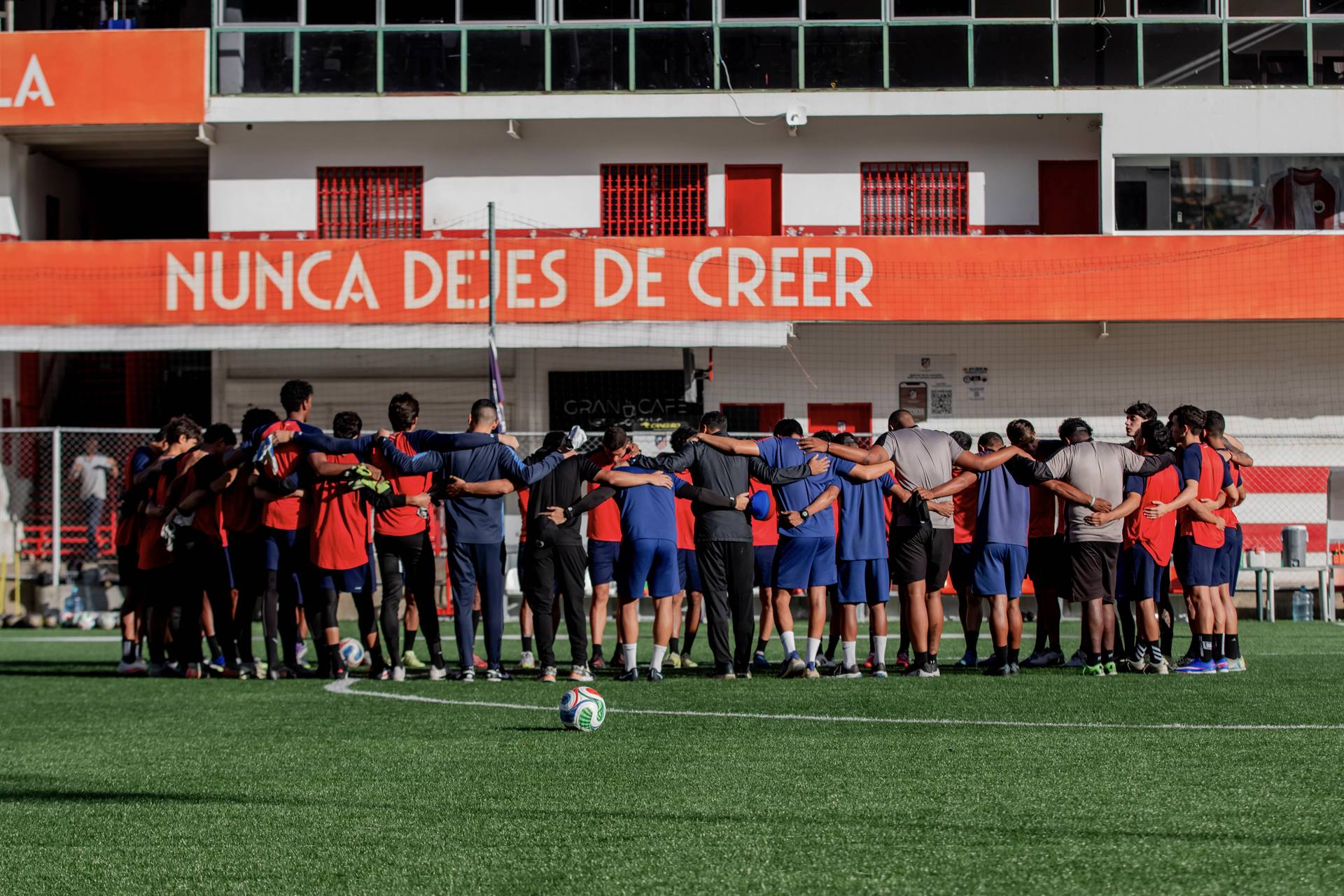 El plantel del Ávila FC reunido en círculo en el campo de La Guacamaya, bajo el cartel Nunca dejes de creer